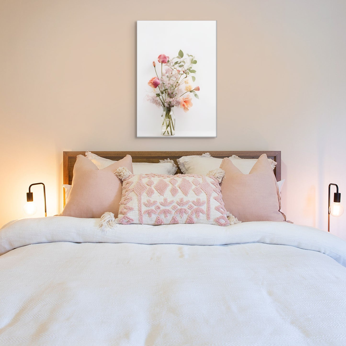 A light and pretty photo of a delicate flower bouquet featuring pink and peach roses, soft green leaves and light purple lilac,. Displayed above a ben with pink and white linens.