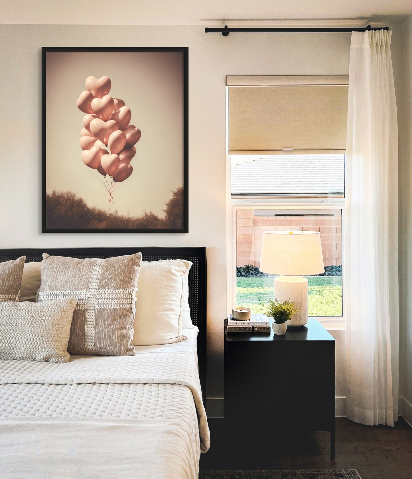 Vintage style photograph of heart shaped balloons. Featuring soft pink balloons floating away in a polaroid style photo. Print on canvas with a black frame displayed over a bed with neutral style colours in the room.