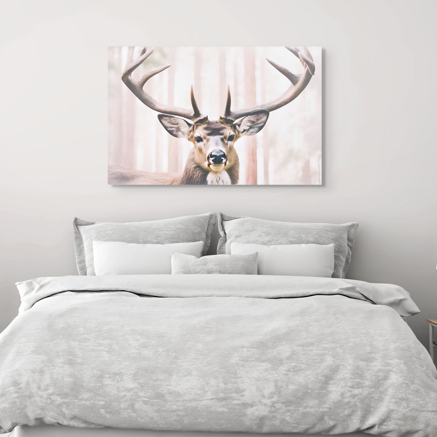 A unique artwork of a deer with long antlers in soft, neutral colors. The background is a light color redwood forest. A print on canvas hung over a bed with white and grey linen.