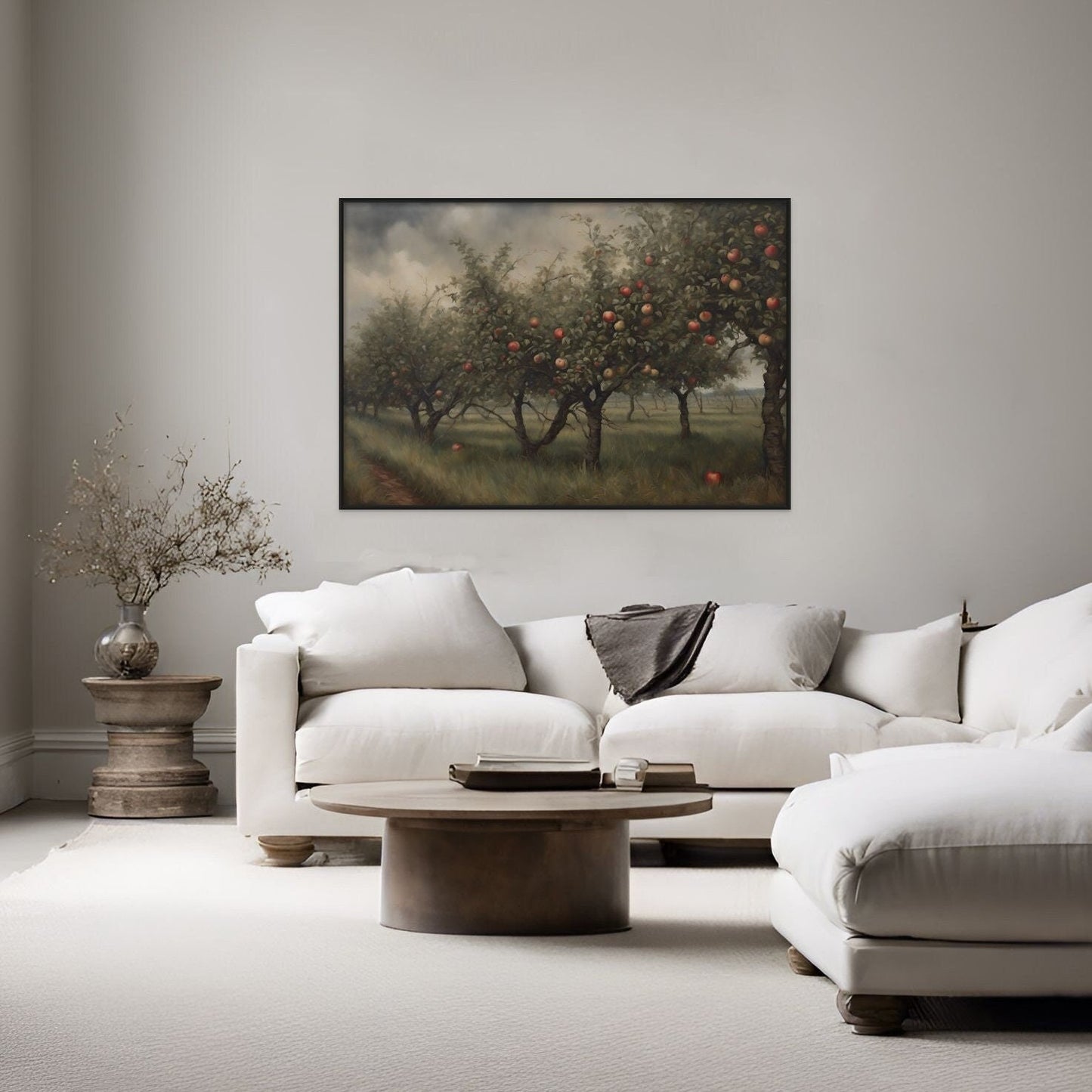 A painting style print of a deep and moody apple orchard displayed above a white couch in a living room.