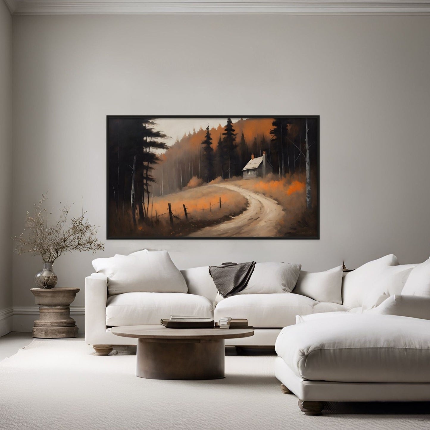 A painting style print of a deep and moody autumn path in the woods. displayed above a white couch in a living room.