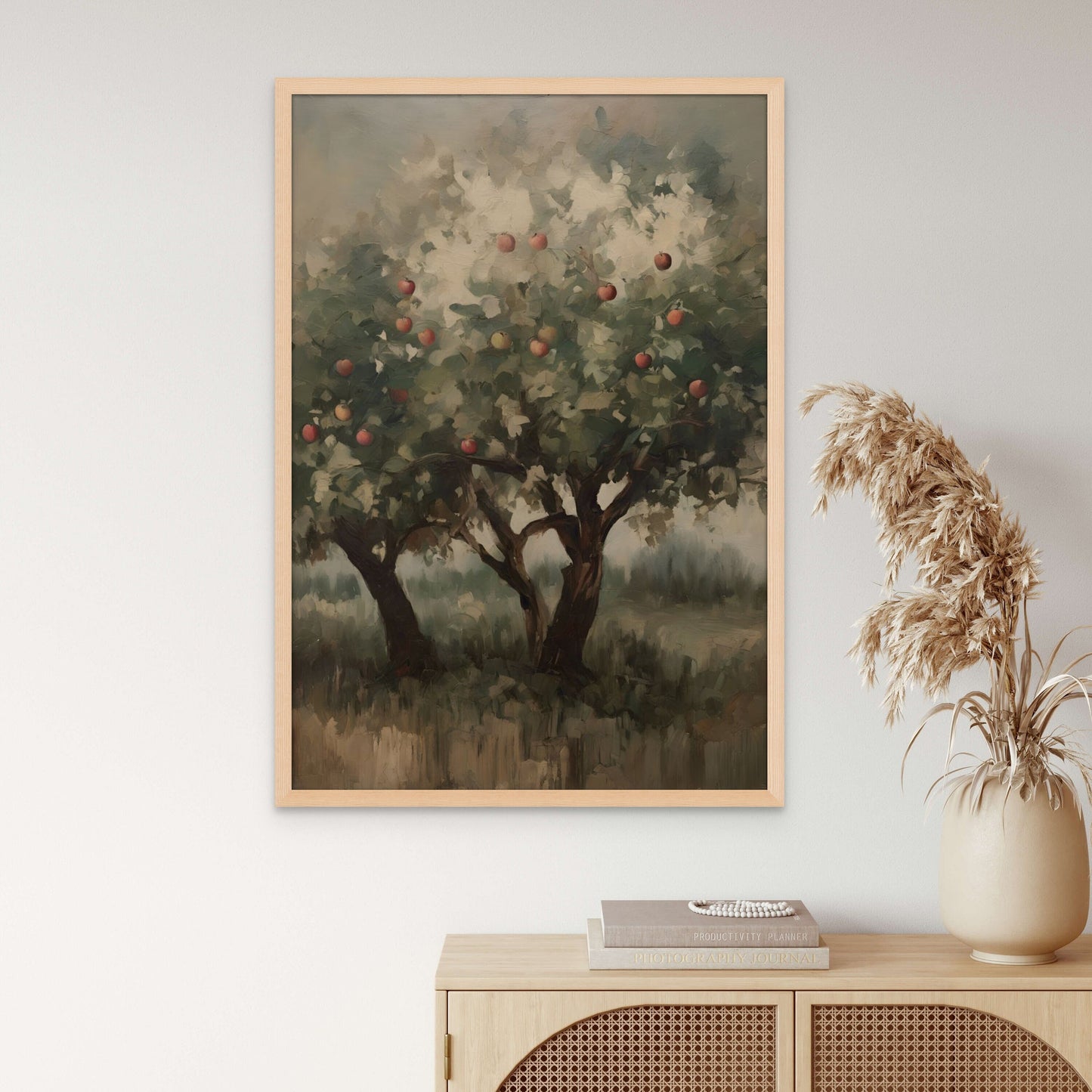 A calming, dark and unique artwork of apple trees. displayed above a light wood hutch and a pampas grass.