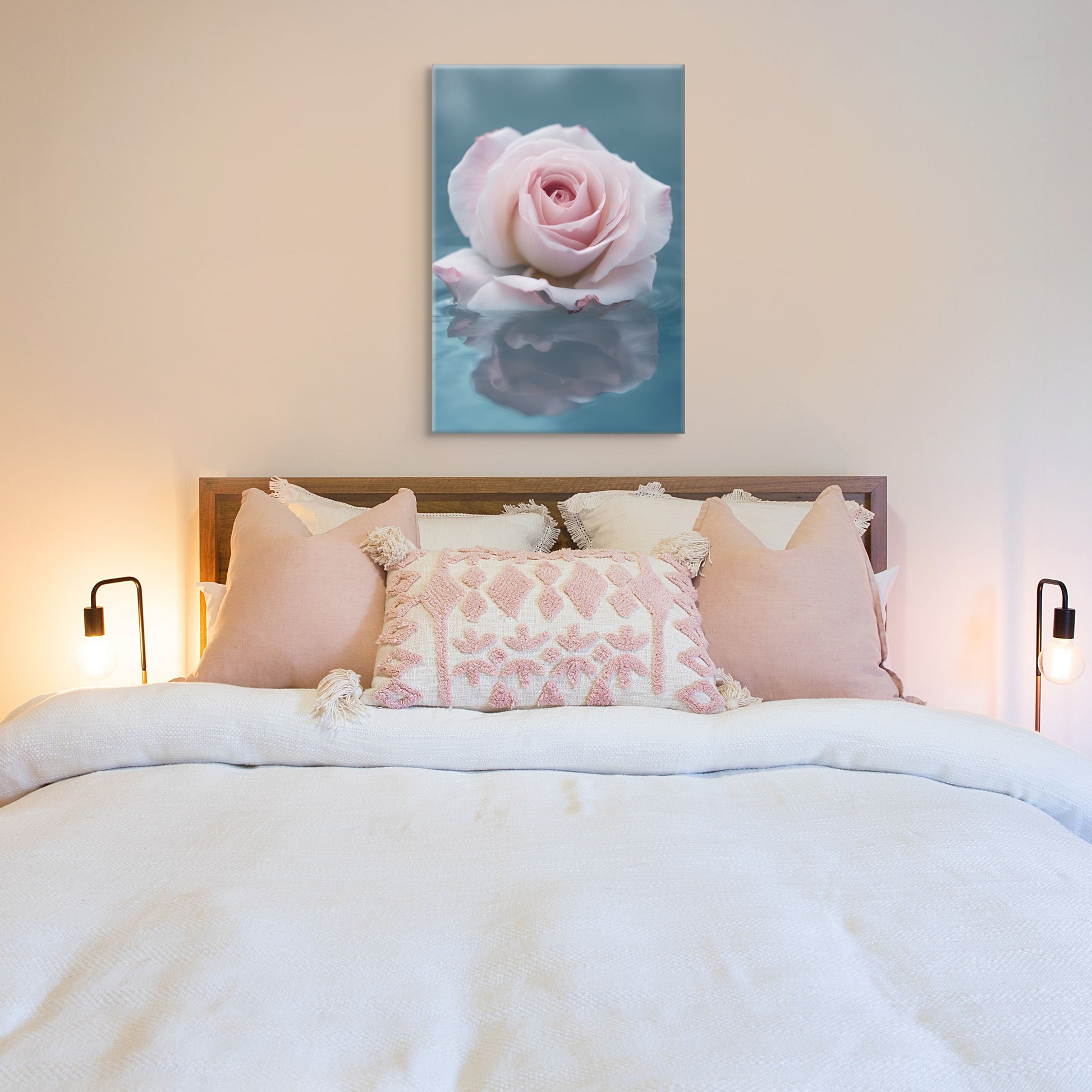 A unique photograph of a soft pink rose floating in soft blue water. It's reflection can be seen in the serene water.  Displayed above a bed that has light pink and white pillows.