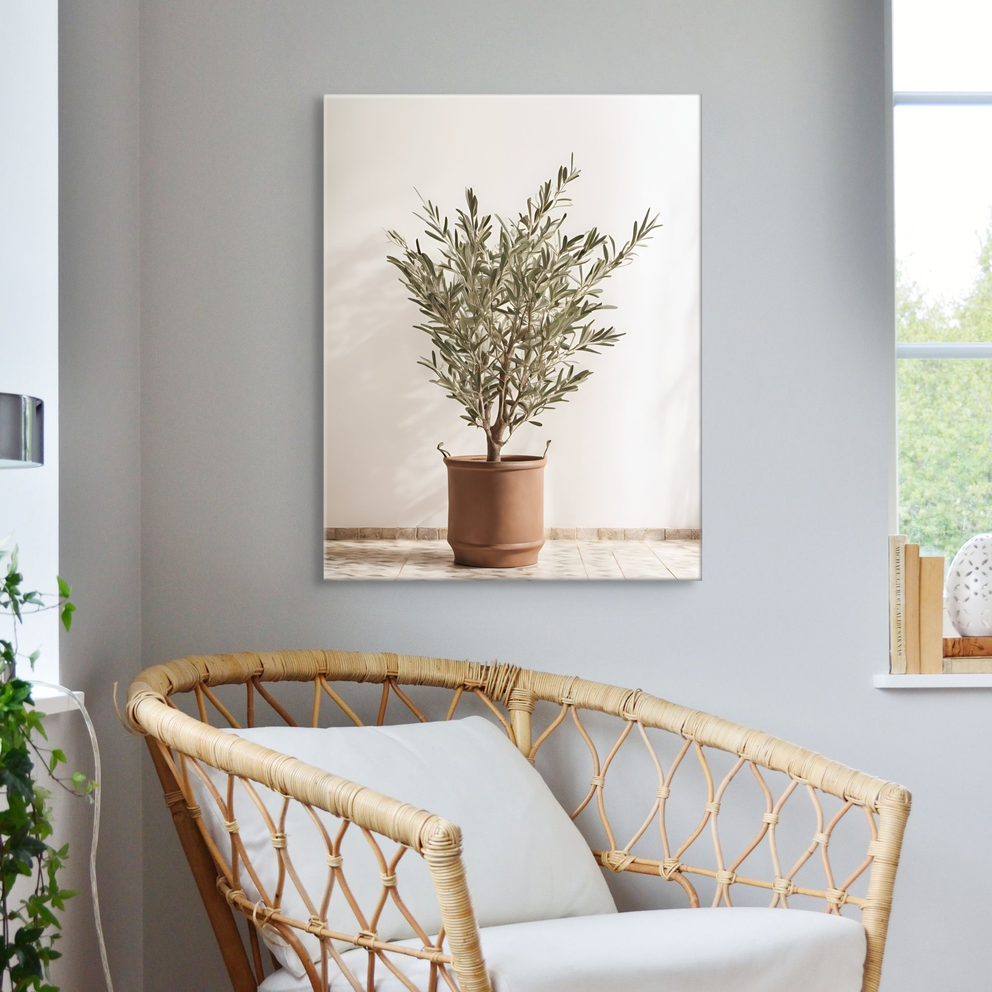 A unique photograph print on canvas of and olive tree in a terracotta color pot with handles. Featuring a bright and sunny background. Displayed over a wicker chair on a grey wall.